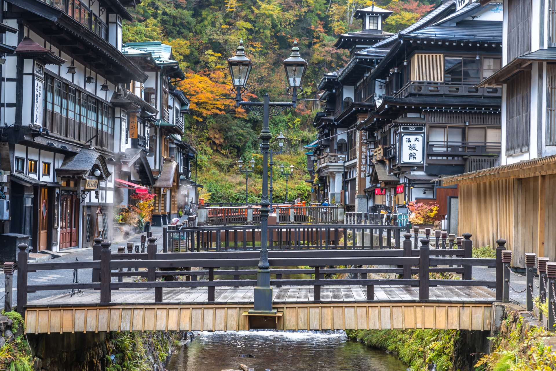紅葉の銀山温泉。川にかかる橋とガス灯、木造の旅館